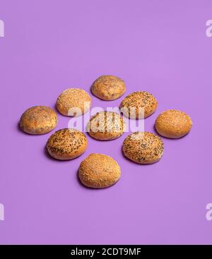 Bread buns symmetrically aligned and isolated on seamless purple background. Hamburger buns with golden crust. Bread rolls with sesame and poppy seed. Stock Photo