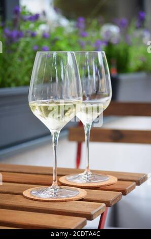 Close up of two glasses of white wine standing on a wooden table, flower pot in background Stock Photo