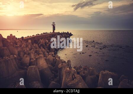 Pier with lighthouse protected by breakwater tetrapods at sunset, color toning applied. Stock Photo