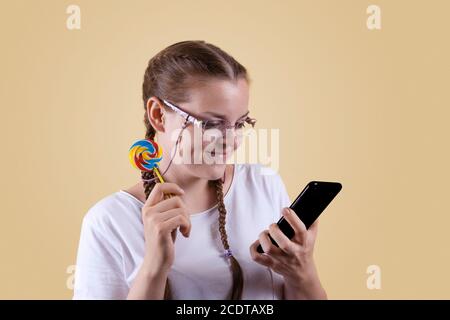 The girl looks at the phone. The girl is holding the phone. Girl with pigtails. The girl is shot against a yellow background.  The girl is surprised b Stock Photo