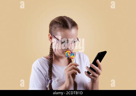 The girl looks at the phone. The girl is holding the phone. Girl with pigtails. The girl is shot against a yellow background. The girl looks thoughtfu Stock Photo