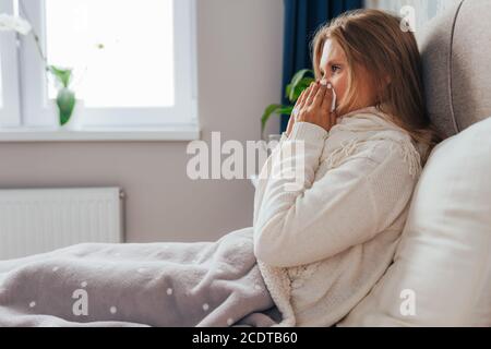 Young woman suffers from influenza at home. Female blows her nose holding tissue handkerchief, having symptoms of chronic sinusitis, seasonal allergy Stock Photo