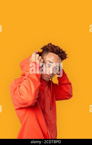 Freestyle. Mulatto guy in hoodie standing isolated on yellow posing to ...