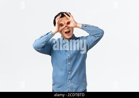 Funny and upbeat, playful asian man making faces, showing fake glasses with hands over eyes, mocking someone, playing, seeing something exciting Stock Photo
