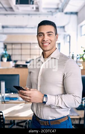 Confident man using smartphone and standing in office Stock Photo