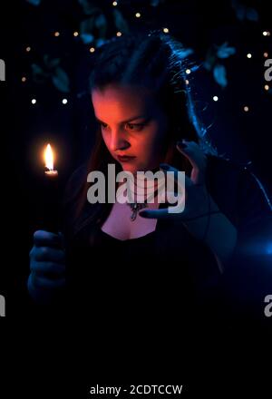 The girl is holding a black burning candle. The girl carefully looks at the candle. The girl is focused on the candlelight. Nice girl in the image of Stock Photo