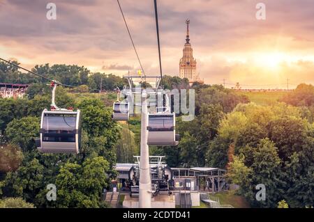 Cable car on Sparrow Hills at sunset, Moscow, Russia. Cableway cabins move over park, main building of Moscow State University in distance. Beautiful Stock Photo