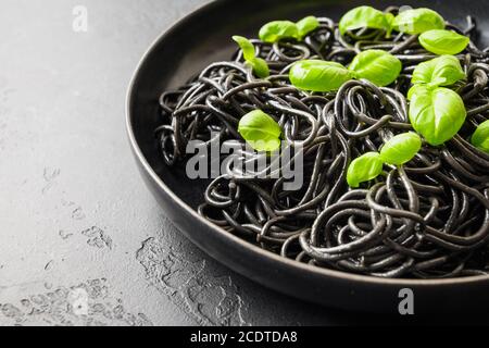 Black pasta spaghetti squid Ink with basil leaves on black background. Top view. Space for text. Stock Photo