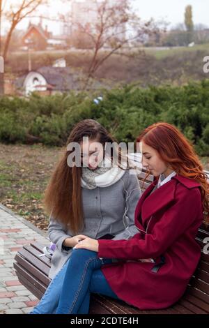 Female teenagers discussing a book sitting on the bench in an autumn city park Stock Photo