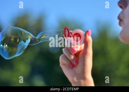Girl blowing soap bubbles outdoor in park on summer sunset. Happiness in nature concept. Close up, selective focus Stock Photo