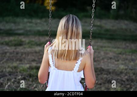 Girl sitting on a swing and holds his hands to the metal chain in the park on a sunny summer day. Relaxation in park concept Stock Photo
