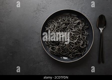 Black pasta spaghetti squid Ink in black bowl on black. Top view. Space for text. Stock Photo