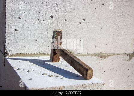 An old hammer on a white foam concrete block from which to build a house from which the shadow falls Stock Photo