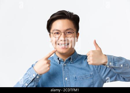 Orthodontics and stomatology concept. Close-up of satisfied asian guy, dental clinic client smiling happy and pointing at his dental braces and Stock Photo