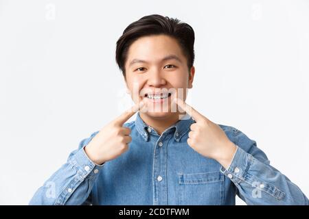 Orthodontics and stomatology concept. Close-up shot of happy smiling asian man recommend dental clinic, pointing fingers at teeth braces with Stock Photo