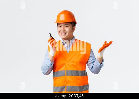 Building sector and industrial workers concept. Smiling confident asian chief engineer, construction manager give orders via walkie-talkie, looking Stock Photo