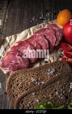 Sliced jerky on a board. Vegetables, bread and meat on the table. Components of a sandwich. Stock Photo