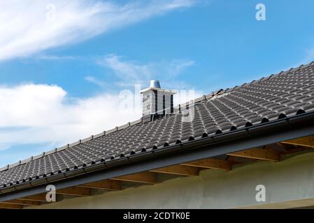 The roof of a single-family house covered with a new ceramic tile in anthracite against the blue sky. Vsible system chimney covered with tiles.