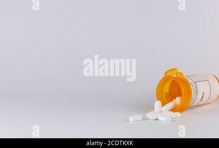 pill bottle lying on its side with white tablet pills spilling out on a white background with copy space in landscape format Stock Photo