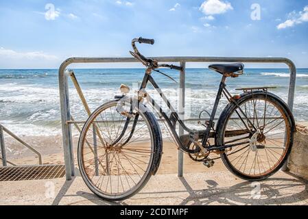 Old retro style abandoned bike parked on a sandy beach on a backgrouns of blue sea Stock Photo