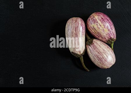 Purple graffiti three eggplants on black stone surface. Top view, copy space. Stock Photo