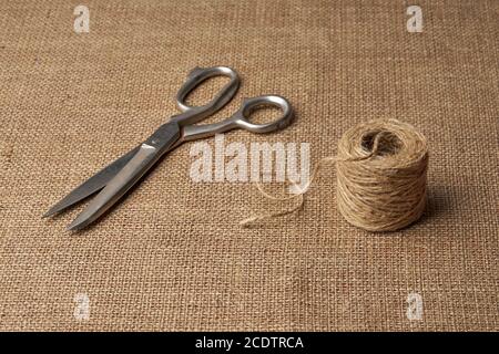 Old steel tailor scissors and skein of jute rope on brown burlap Stock Photo