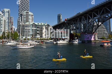 Sailboats, a passenger ferry and paddle boaters move across False Creek and past the Granville Street bridge and downtown apartments and condominiumns Stock Photo