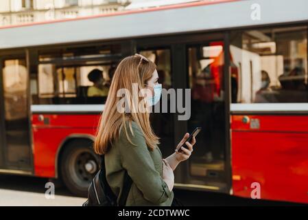Girl with mask holding a phone, bus in background Stock Photo