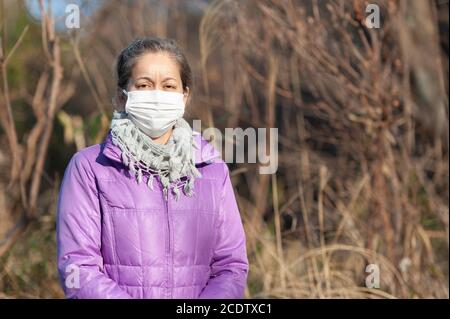 Beautiful mixed race middle aged woman wearing a white mask for protection against Coronavirus (COVID-19) and other infectious diseases. Front view. Stock Photo