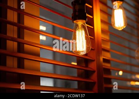 Shining golden antique Edison style bulbs in the restaurant. Lighting decor concept. Vintage light bulb. Blur window jalousie background Stock Photo