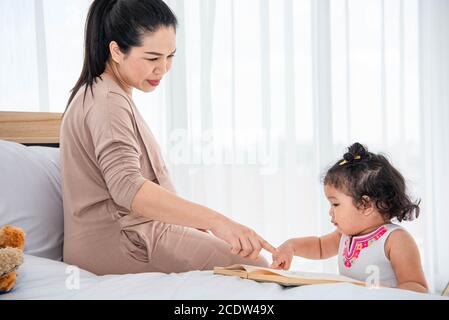 Asian mother teaching girls daughter to reading books in house. Quarantine in home concept. Happy family theme. Stock Photo