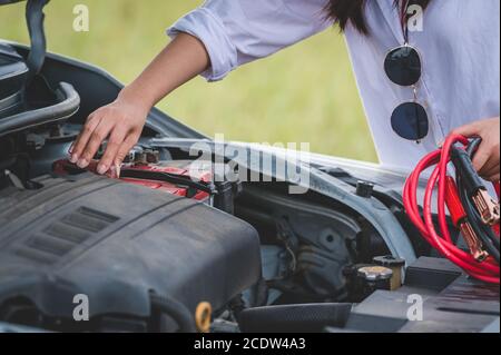 Closeup of woman hand holding battery cable copper wire for repairing broken car by connect battery with red and black line to electric terminal by he Stock Photo