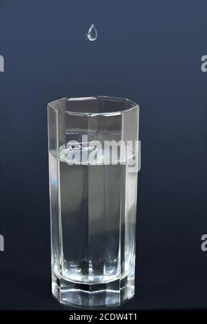 Drop of water falling into a glass filled with drink Stock Photo
