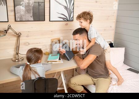 Little boy embracing his father by neck while standing on bed behind him Stock Photo