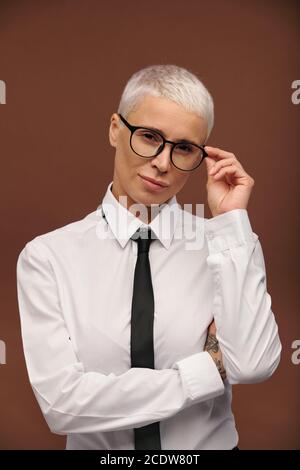 Young serious masculine female in formalwear touching her eyeglasses Stock Photo