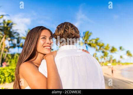 Couple hugging on tropical beach Asian woman holding man looking away pensive. Beautiful girlfriend happy smiling at sunset with boyfriend Stock Photo