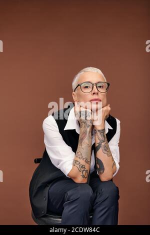 Young blond woman with short hair and arms covered with tattoos sitting on chair Stock Photo