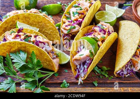 salmon tacos with red cabbage salad with spicy yogurt sauce sprinkled with finely chopped parsley served on a rude cutting board on a dark wooden tabl Stock Photo