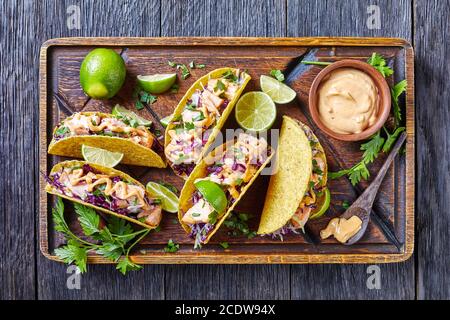 salmon tacos with red cabbage salad with spicy yogurt sauce sprinkled with finely chopped parsley served on a rude cutting board on a dark wooden tabl Stock Photo