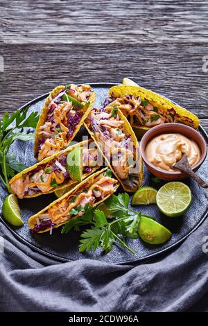 close-up of salmon tacos with red cabbage salad with spicy yogurt sauce sprinkled with finely chopped parsley served on a black plate on a dark wooden Stock Photo