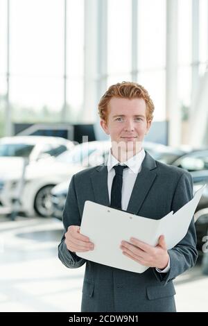 Young manager of contemporary car center holding open folder with documents Stock Photo