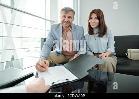 Contemporary middle aged couple signing document of selling and buying new car Stock Photo