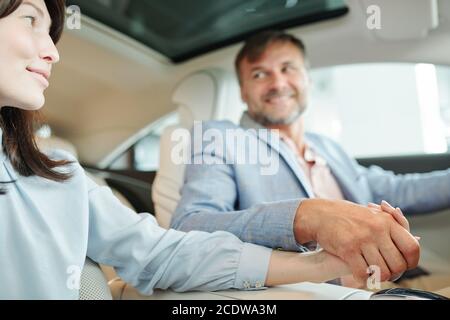 Hands of contemporary affectionate middle aged couple sitting on backseat of car Stock Photo