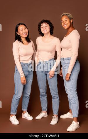 Three young intercultural joyful women looking at you with toothy smiles Stock Photo