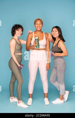 Three young laughing sportswomen holding bottle of water and dumbbells Stock Photo