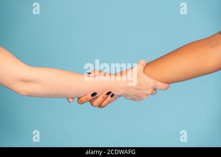 Hands of young females with white and dark skin holding by each other Stock Photo
