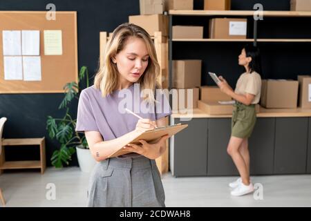 Serious young blond female manager of online trading office making notes Stock Photo