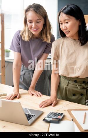 Two happy young businesswomen in casualwear looking at laptop display Stock Photo