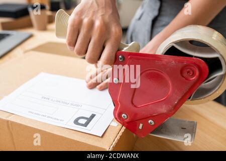 Hand of female manager of online shop with cellotape gun dispenser sealing box Stock Photo