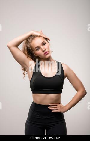 Fit young woman in black tracksuit touching her long blond curly hair Stock Photo